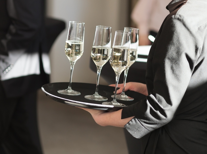 Eine Servicekraft trägt ein Tablet mit Sektgläsern.
